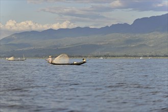 Tranquil scene with a fisherman on his boat, green mountains in the background, Inle Lake, Myanmar,