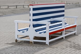 A large, empty beach chair with red, blue and white stripes stands on a cobbled path, Zeebrugge,