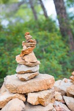 Carefully stacked, slightly red stones form a stone figure, cairn, waymark, marker in the forest,