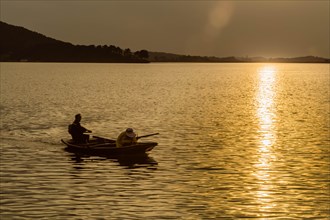 Two fishermen on a boat in a lake during sunset, framed by golden light and calm waters, in South