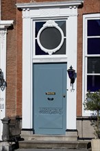Elegant blue door with oval window on a historic building with lantern next to it, Middelburg,