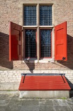 Historic window with red shutters and a matching bench in front of it