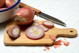 Sliced shallots on a wooden board with a knife, Allium cepa