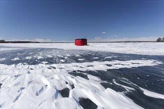 Winter, red fishing hut with snow drifts on a frozen riverscape, Saint Lawrence River, Province of