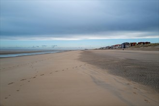 Disused beach with dunes in the background and houses on the horizon under a cloudy sky, DeHaan,