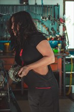 Young confident skilled hispanic Mechanic woman is closely examining a vehicle part in a garage