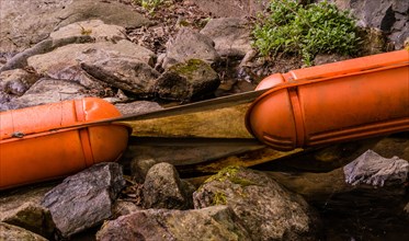 Closeup of two large orange floats discarded in a woodland stream surrounded by rocks and boulders