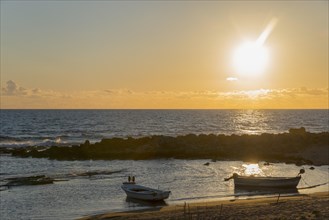 A peaceful sunset by the sea with boats and rocks in the golden light of the evening sun,