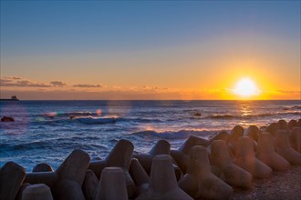 Amber sky during sunrise over sea with tetrapods and soft waves hitting the shore, in South Korea