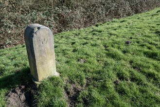 Old stone pillar with inscribed date in the grass at the edge of the path
