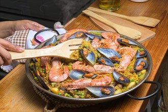 A person serving seafood paella with a wooden spatula from a traditional pan, typical Spanish