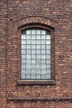 An arched window with glass bricks in a detailed brick wall