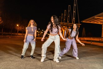 Group of three young freestyle dancers performing in the street at night in summer