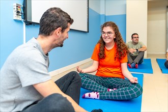 Yoga instructor and disabled woman talking while practicing yoga sitting on a mat with other people