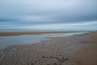 Wide beach with puddles of water and sandbanks, covered by a cloudy sky, DeHaan, Flanders, Belgium,