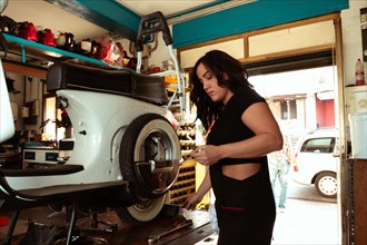 Sexy woman confident Mechanic in black attire fixing a tire on a white scooter in a workshop,