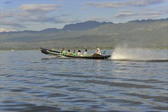Motorboat with passengers racing on a calm river with mountain backdrop, Inle Lake, Myanmar, Asia