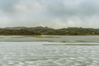 Serene but desolate winter scene with a river covered in sheets of ice and surrounded by hills, in