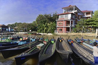Moored boats on the bank of a river with a large building in the background, Inle Lake, Myanmar,