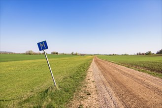 Long straight dirt road in the countryside towards the horizon with a meeting place sign at the