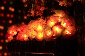 Glowing round paper lanterns on display at a market with soft, warm lighting and bokeh background.
