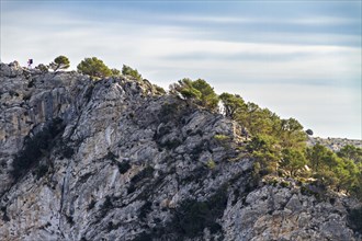 Hikers on the edge of a cliff with a backdrop of trees and clear skies, Hiking tour in Taix massiv,