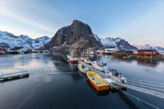 A fishing harbor with boats docked and mountain in the background at dawn, Lofoten