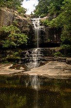 Gentle waterfall with its reflection visible in the clear, still water below, encased by forest, in