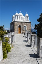 A white path leads to a church with blue domes under a bright blue sky, Byzantine fortress with