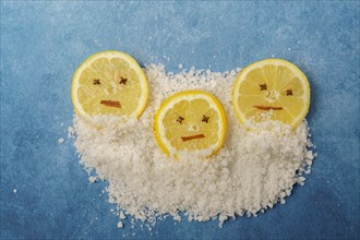 Lemon slices with cloves and cinnamon forming a smiley face on a pile of salt and blue background