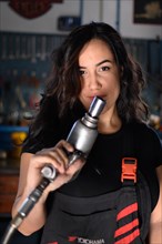 Playful confident woman mechanic holding an air hose and making eye contact in a workshop, a