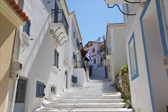 A sun-drenched alleyway with white houses and blue accents in Koroni, Pylos-Nestor, Messinia,