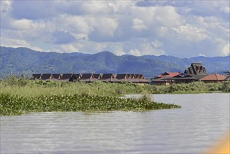 Tranquil river landscape with traditional huts against a mountain backdrop, Inle Lake, Myanmar,