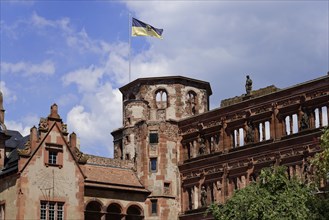 Part of a castle (Heidelberg Castle), with a waving flag on the tower against a cloudy sky,