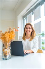Vertical photo of a female elegant real estate agent using laptop sitting on a desk