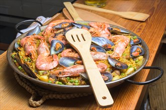 Seafood paella ready to be served with a wooden spatula on the table, typical Spanish cuisine,