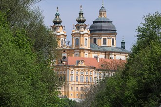 Baroque abbey surrounded by green trees with gold-decorated towers and dome under a blue sky Melk