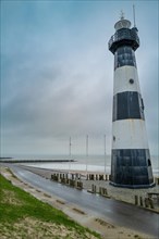 Black and white lighthouse on the coast with grass and sand under a cloudy sky, Breskens, Zeeland,
