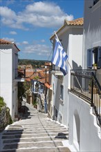 A narrow alley with a staircase between traditional white houses under a blue sky, Koroni,