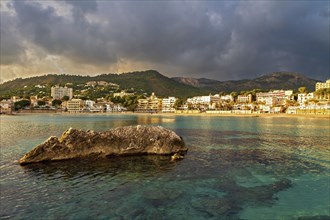 Coastal town by the sea at sunset with golden clouds and a large rock in the water, Peguera,