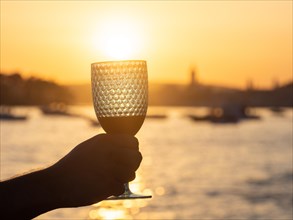 Tourist holding wine glass against the light, sunset over the town of Rab, island of Rab, Kvarner