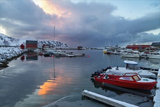 Twilight scene at a snow-covered harbor with boats and a vibrant sky reflection in the water,