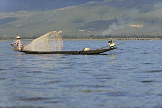 Fisherman enjoying the sun rays while working, surrounded by a mountain landscape, Inle Lake,