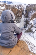 A woman meditating in winter in Iceland at the frozen Hengifoss waterfall
