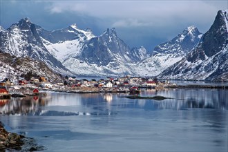 Peaceful fjord with fishing village, snow-covered mountains reflected in still water, Lofoten