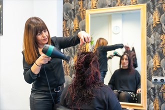 Woman facing a mirror while a hairdresser drying her hair in the hair salon