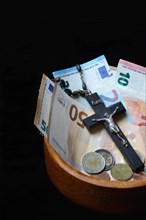Crucifix and banknotes in a bowl, church and money, church tax