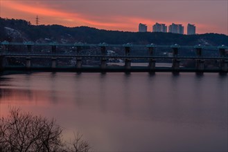 Sunset over a river dam with silhouette of distant buildings, in South Korea