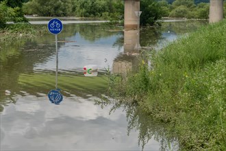 Round sign says BICYCLE PATH in Korean, with trees submerged in flooded river after torrential