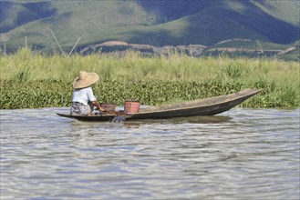 Person steering a traditional boat on a calm river with mountain panorama, Inle Lake, Myanmar, Asia